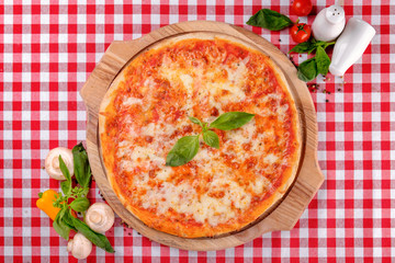 Neapolitan Margherita pizza with mozzarella cheese, basil, vegetable and tomatoes sauce, served on a wooden board for a dinner in italian restaurant background, top view. Italy food. 