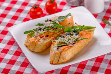 Italian Appetizer Bruschetta with Salmon, parmesan, balsamic vinegar and fresh arugula on white plate in italian restaurant background, top view.