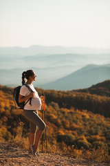 Pregnant woman nordic walking with trekking sticks on hill with beautiful autumn mountain view. Pregnancy activity and healthy lifestyle in maternity time. Travel concept. - 373417179