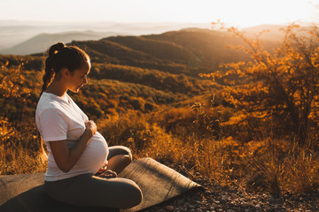 Spiritual and emotional concept of harmony with nature in maternity time. Pregnant woman practicing yoga outdoors on hill at sunset. Amazing autumn mountain view. - 373417392