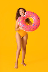 Beautiful young African-American woman with inflatable ring on color background