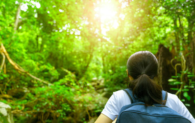 Happy asian woman with backpack travel in green forest. Adventure travel. Minimal life. Back view of black long hair woman with white shirt in tropical forest for vacation. Active girl in the woods.