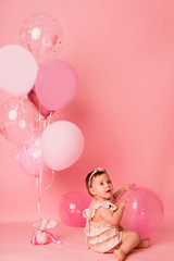 Happy baby girl on a pink background with balloons. Celebration. Birthday
