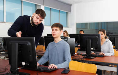 Fototapeta na wymiar Portrait of adult teacher helping young male student in computer class in university