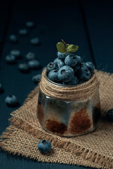 Metal bowl with wet ripe blueberry on burlap napkin and dark wooden table.