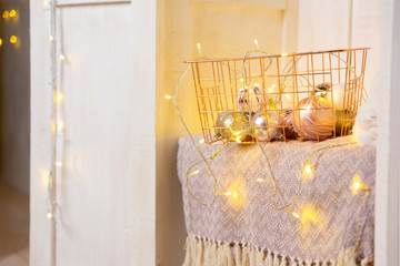 Gold metal basket on a shelf in a white wooden cabinet or wardrobe. Garland, Christmas toys and balls in a basket. New Year or Christmas background. Postcard and greeting card.