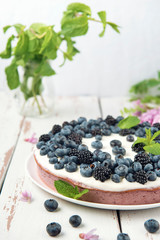 Cottage cheese casserole with blackberry and blueberry on white Provence style table. Sweet pie with acacia flowers and mint leaves on white backdrop.