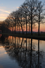 Fototapeta na wymiar Panorama of a gorgeous scenic sunset at a river or canal, with gold and blue color in the sky and the line of trees reflected in the water. High quality photo