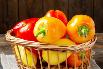 Bell pepper. Red, yellow and orange peppers in a basket on a brown wooden table. Paprika close up	