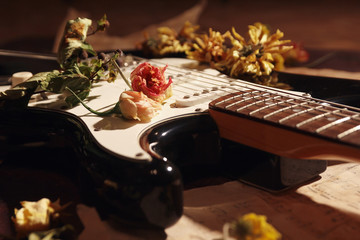 Dried flowers and electric guitar on vintage music notes close up. Selective focus.