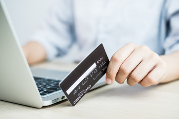 The businesswoman's hand is holding a credit card and using a laptop for online shopping and internet payment in the office