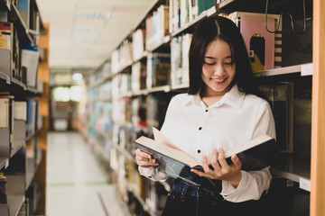 Young Asian women are searching for books and reading from the bookshelves in the college library...