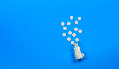 White tablets and a glass bottle on a blue background. Concept of healthcare and medicine. Flatley. The view from the top. Space for text.