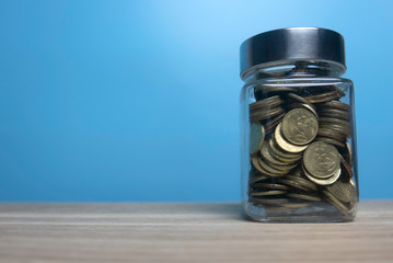 Selective focus jar full with gold coins  and copy space on wooden table with a blue background.