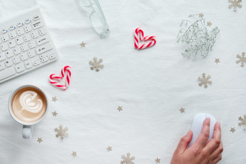 White style top view, computer workspace and female hand on mouse. WIntertime flat lay with coffee cup, hearts from candy canes, paper decor.
