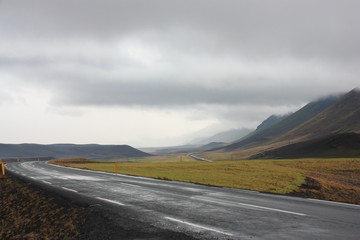 An empty winding road in the volcanic mountains of Iceland on a cloudy day