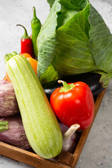 Assortment of vegetables in a wooden box. There are many different raw vegetables in the box. Cabbage, zucchini, garlic, sweet pepper and eggplant on the table. Healthy food concept
