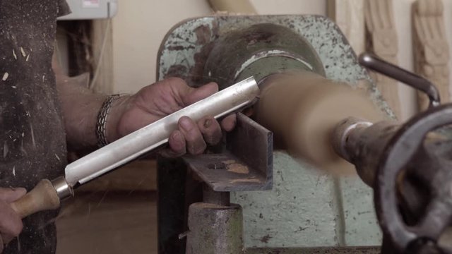 Carpenter uses skew chisel at workshop. Professional craftsman shaping piece of wood on wood turning lathe.