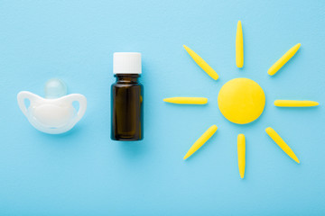 Brown bottle of d vitamin, white soother and yellow sun shape on light blue table background....