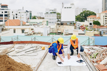 Engineers in hardhats discussing blueprint when working at building under construction