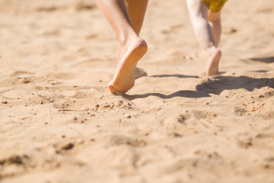 Young mother and baby legs walking synchronous together on sand at beach in sunny summer day. Back view. Closeup.