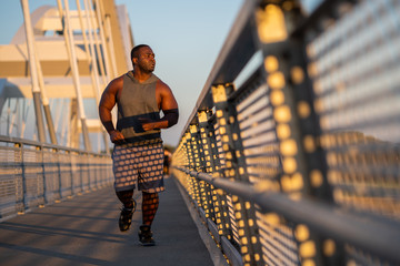 Young african-american man is jogging  on the bridge in the city.