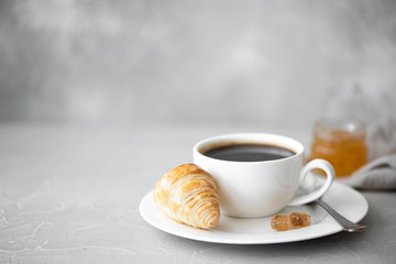 a cup of black coffee with croissant and jam