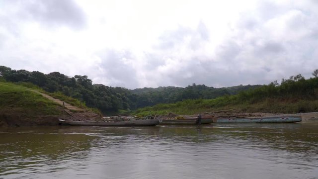 wood canoes floating in dark river attached to green land and cloud above them. pan shot.par2