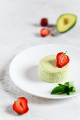 Avocado panna cotta with strawberry pieces and mint leaves on a white plate. Sugar, lactose, gluten free. Healthy food, diet, vegetarian.