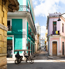 Road in old Havana with green car in front of colorful buildings with rickshaw.