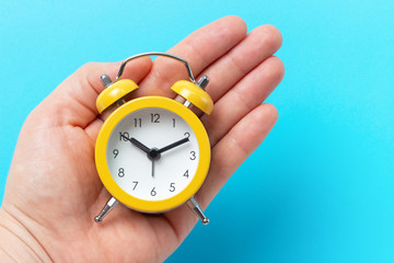 Hand holds yellow alarm clock on blue background, copy of space