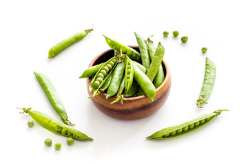 Green pea pods in wooden bowl on the kitchen background