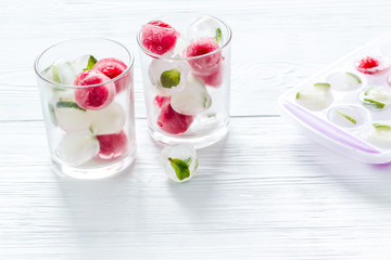 Cocktail glasses with berries in ice cubes on white table