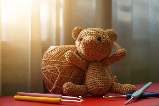 Handcrafted cute crochet brown bear doll using polyester yarn, amigurumi knitted bear doll with crochet hooks on red table