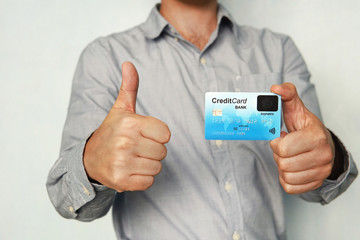 Man holding credit card with built-in fingerprint scanner and showing thumb up. Concept of safe...