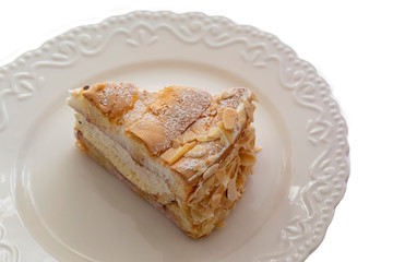 Sponge cake with cream sprinkled with nuts on a white plate and background.