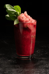 Refreshing ice smoothie strawberry and basil cocktail in a transparent glass glass on a black background.