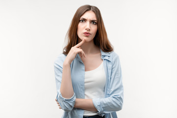 Thoughtful young woman with long chestnut hair looking Seriously at camera and holds a finger to his face