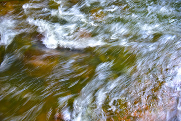 Background of clean water in fast river flow. Fast flow in mountain creek. Texture of the fast river natural water surface. Motion, soft focus
