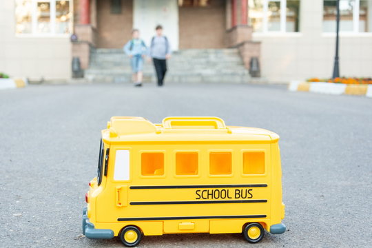 In the foreground is a yellow toy school bus, with children running towards it in the background. back to school concept.