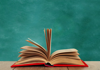 Open book textbook in a red cover on a wooden desk on the background of a green school chalkboard. Back to school distance home education.Quarantine concept of stay home.