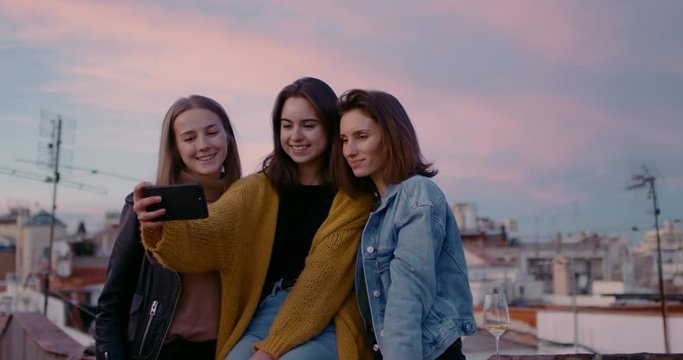 Cute tourist girls making selfie and posing during the golden hour with an old city on their background. With soft evening pink sunset light. Slow Motion