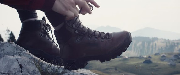 Woman sit on rock tighten shoelaces on hiking or mountaineering boots or shoes footwear on autumn or fall hike unrecognizable slow motion close up morning at Velika Planina in Slovenia Alps
