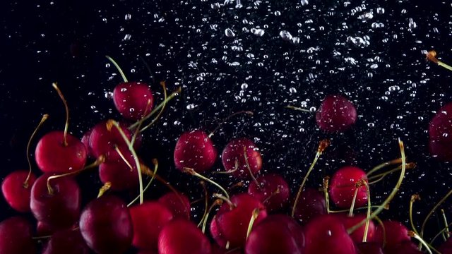 Cherries falling down in to the water. Lots of cherries falling slowly on a black background. Organic fruit  isolated on black background. Fresh water with fruits.