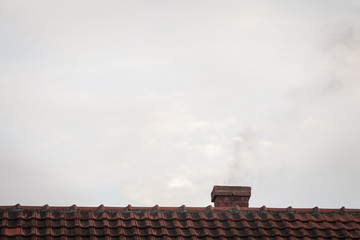 brick chimeny on the roof of an individual residential house with tiles exhausting little fumes at dusk, during a sunny afternoon