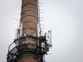 Mobile phone base station, on an old industrial brick chimney equiped with 3G, 4G and 5G antenna, at the top of a European building, used for cellular phone coverage, reception and transmission