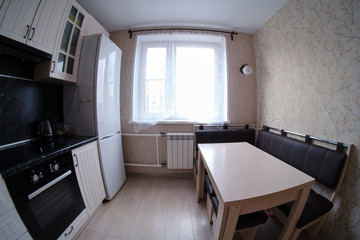 Kitchen white with black color and wooden table (fisheye photo). Laminate floor, black countertops and light window