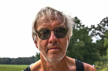 Portrait of a senior man with sunglasses in which the reflection of the photographer can be seen.