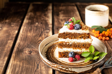 A piece of carrot cake decorated with berries and figs on a wooden background. Traditional donkey pastries. Copy space.