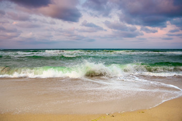 dramatic weather on the seashore. green waves crashing on the beach. cloudy purple sky in evening light